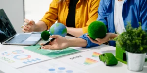 Un grupo de personas analiza documentos y gráficos relacionados con sostenibilidad, mientras manipulan objetos verdes que evocan la naturaleza, en el contexto de la elaboración de Reportes ESG.